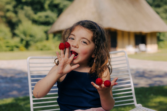 Meisje zit in stoel en eet aardbeien uit het vuistje